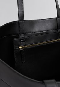 Μαύρη δερμάτινη τσάντα ώμου με λεία υφή, ανθεκτικές διπλές λαβές και εσωτερική τσέπη με φερμουάρ και χρυσά μεταλλικά στοιχεία.