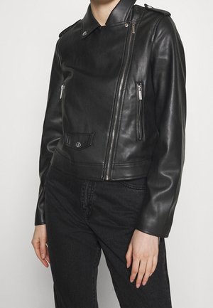 Schwarze Leder-Bikerjacke mit asymmetrischem Frontreißverschluss, Reißverschlusstaschen und geknöpftem Kragen, getragen zu schwarzen Hosen.
