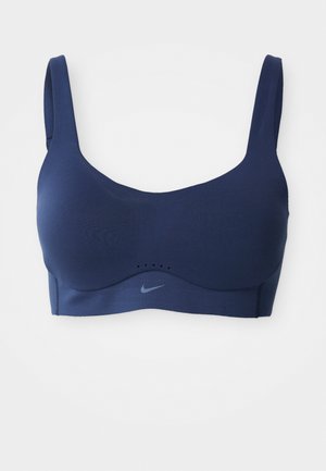 Tumed sinine spordirinnahoidja, millel on laiad rihmad, sile tekstuur ja diskreetne Nike logo. Omab ventilatsiooniavasid, et tagada õhuniiskus.