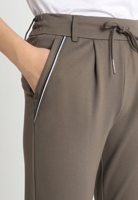 Grijze joggerbroeken met een trekkoord in de taille, plooien en zijzakken met witte bies. Gladde textuur en casual ontwerp.