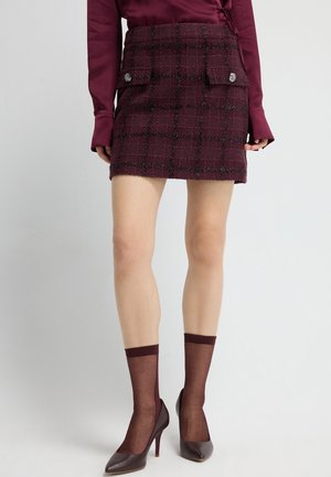 Bordeaux tweed mini-rok met ruitpatroon, voorzien van twee voorzakken en decoratieve knopen. Draag het met doorschijnende bordeaux sokken en hakken.