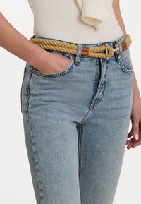 Repbälte i beige med bruna läderdetaljer, bärs över ljusblå högmidjade jeans med två sidofickor och en skräddarsydd passform.