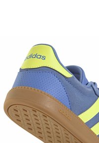 Zapatilla Adidas en azul y amarillo con parte superior de cuero texturizado, franjas en contraste y una suela de goma con un patrón de cuadrícula.