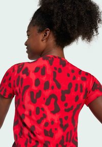 Camiseta roja con estampado de leopardo negro, de manga corta, con cuello redondo y textura de tela suave, mostrada desde un ángulo lateral y trasero.