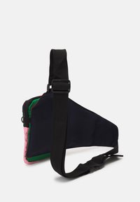 Torba na jedno ramię o trójkątnym kształcie, wykonana z granatowej tkaniny z różowymi i zielonymi akcentami, regulowanym czarnym paskiem oraz zamknięciem na zamek błyskawiczny.