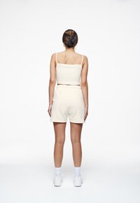Top sin mangas ajustado color crema y shorts a juego, hechos de una tela suave, con cintura elástica y un corte relajado. Zapatillas blancas completan el look.