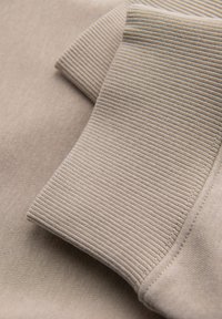 Gros plan d'un poignet en tissu côtelé beige cousu sur une manche lisse d'un vêtement beige.