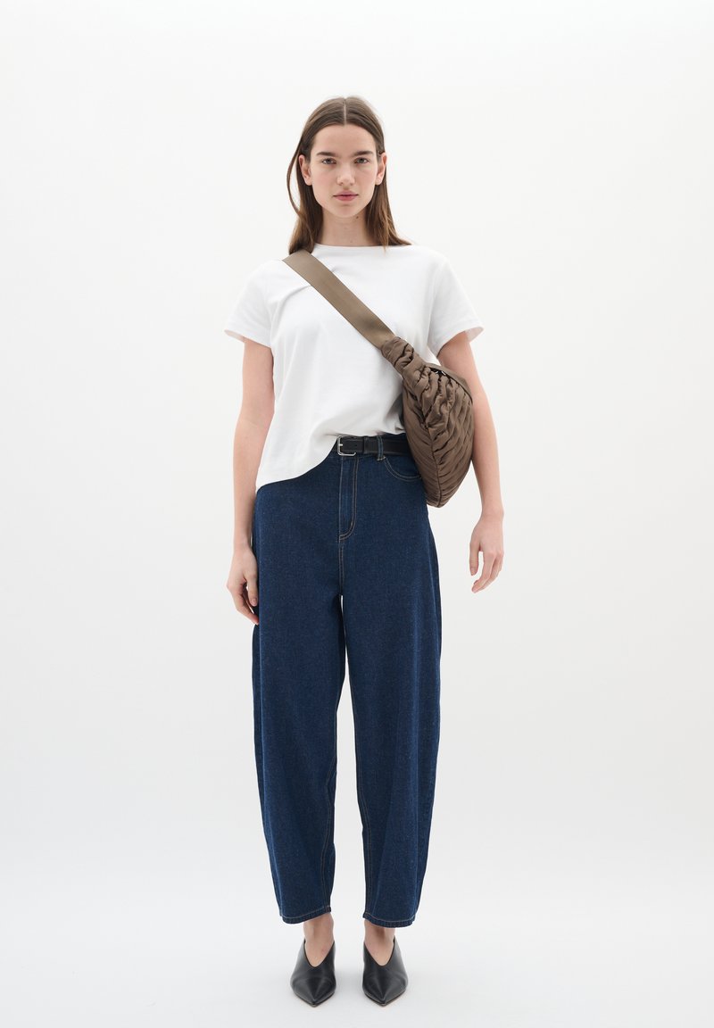 T-shirt bianca in cotone, pantaloni di denim scuri a gamba larga, borsa a spalla intrecciata marrone scuro e scarpe nere a punta. Design semplice e moderno.