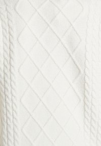 Tissu tricoté blanc avec motifs en forme de diamant et câbles torsadés, créant un design géométrique texturé.