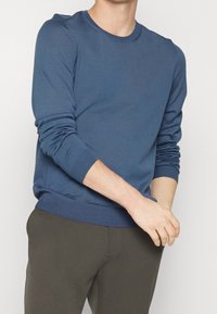 Modrý svetr s kulatým výstřihem vyrobený z měkkého materiálu, s dlouhými rukávy, žebrovanými manžetami a lemem, s hladkou texturou a přiléhavým střihem.