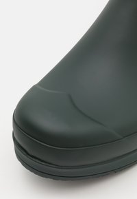 Green waterproof boot with a rounded toe and smooth rubber texture. The design features a thick sole and minimal detailing.