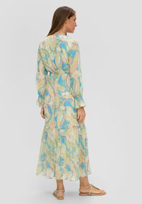 Langes, gestuftes Kleid aus leichtem Stoff mit einem blau-gelben und pinkfarbenen Paisleymuster. Mit langen Ärmeln und Rüschensaum.