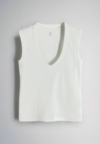 White sleeveless knit top with V-neck, ribbed texture, and a tag at the neckline reading "THE SET, Made in Korea" against a plain background.