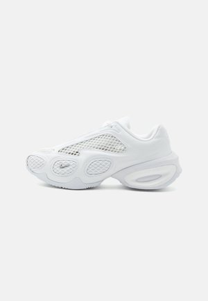 Biely športový teniska so sieťovinovými panelmi, zaobleným dizajnom podrážky a malým logom Nike blízko špičky na jednoliatom svetlom pozadí.