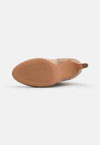 Botines de ante color marrón claro con puntera redonda, exterior texturizado y suela de goma flexible con un patrón ondulado. Lengüeta en el talón para facilitar el uso.