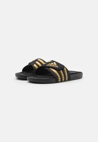 Sorte rastegner med en teksturert såle, gull tre-stripes design og preget "adidas"-merke på stroppen for ekstra detaljer.
