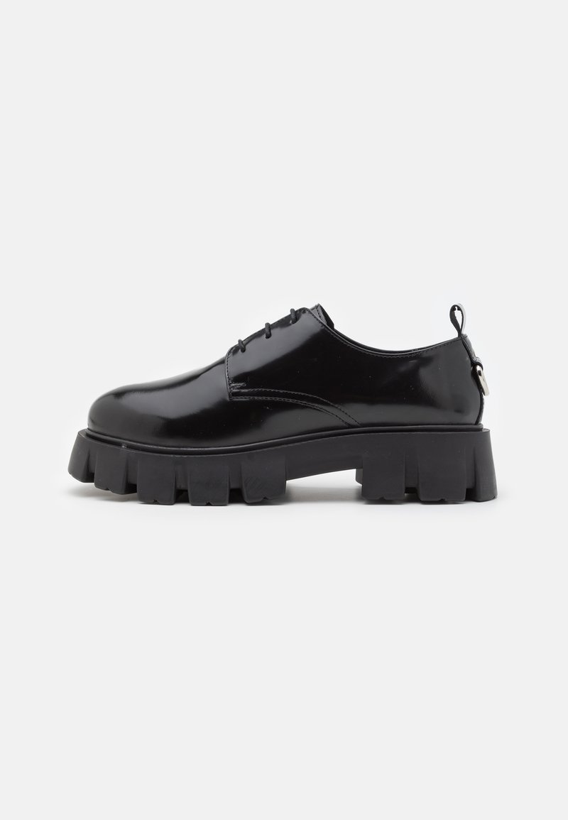 Scarpe in pelle verniciata nera con una suola in gomma nera spessa e strutturata. Caratterizzate da una punta arrotondata, design con lacci e una piccola linguetta sul retro.