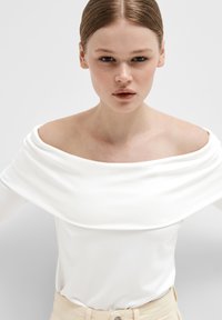 Hvit, off-shoulder langermet topp med drapert hals, glatt tekstur, kombinert med beige bukser, enkel og elegant design.