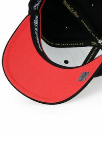 Black cap with a red brim. Interior features grey lining and gold text detailing. Includes embroidered branding and ventilation holes.