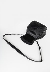 Borsa in pelle nera con una texture morbida, patta pieghevole e chiusura magnetica. Presenta spallacci sottili e regolabili e un interno in suede.