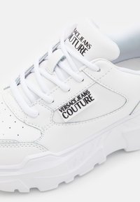 Baskets blanches en cuir et mesh, avec une semelle en caoutchouc épaisse, un embout perforé et le logo "Versace Jeans Couture".