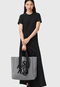 Borsa tote grigia con un design grafico in nero, dotata di robusti manici neri e di una forma elegante e strutturata. Materiale opaco con superficie testurizzata.