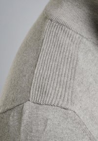 Grauer Pullover mit einer Mischung aus glatten und gerippten Texturen, rundem Ausschnitt und kantigen Nähten, die kontrastierende Strickmuster präsentieren.