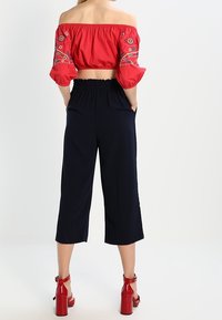 Röd off-shoulder topp med blommig broderi, tillsammans med marinblå cropped byxor och röda högklackade skor. Slätt tyg och elastisk midja.