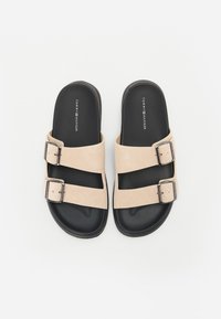 Beige semskede sandaler med to justerbare stropper, sølvspenner og en svart gummisåle. Merkevarenavnet er trykt på fotsengen.