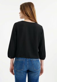 Zwarte blouse met 3/4 mouwen, puffed sleeves en een ronde halslijn; gemaakt van lichtgewicht stof. Draag het met blauwe spijkerbroeken.
