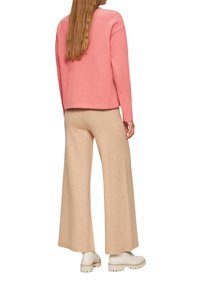 Roze sweatshirt met een ontspannen pasvorm, gecombineerd met beige wijdere broeken. Het model draagt witte schoenen met een chunky zool. Zachte texturen zijn duidelijk zichtbaar.