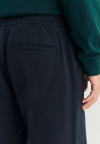 Marineblauwe broek met een elastische tailleband, een platte achterzak en een gladde textuur. Het kledingstuk oogt lichtgewicht en casual.
