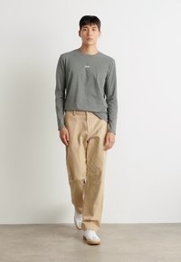 Graues Langarm-T-Shirt mit Logo, beigefarbene Hose und weiße Sneaker. Einfaches Design, lockere Passform, aus leichtem, glattem Stoff.