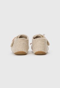 Chaussons en feutre beige avec un dessus en textile doux et une forme ronde. Dotés d'une sangle à velcro et d'une semelle en caoutchouc texturé.