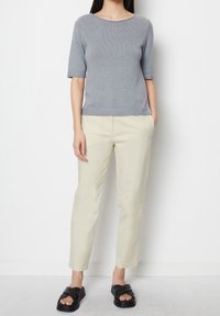 Szary dzianinowy sweter z krótkim rękawem i ściągaczami, zestawiony z jasnobeżowymi spodniami typu tapered oraz czarnymi klapkami z krzyżującymi się paskami.