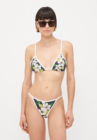 Sötét virágmintás bikini szett fehér virágokkal és zöld levelekkel, fehér pántokkal kiegészítve és minimalista dizájnnal.