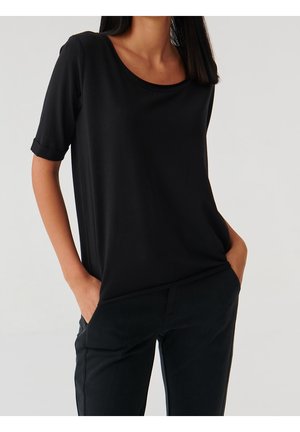 Czarny top z krótkim rękawem i okrągłym dekoltem, wykonany z gładkiej tkaniny. Charakteryzuje się podwiniętymi rękawami i luźnym krojem. Noszony z czarnymi spodniami.