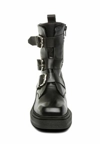 Bota de tobillo de cuero negro con tres hebillas de plata ajustables, punta redonda, parte superior texturizada y suela gruesa negra.