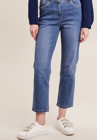 Blauwe denim jeans met een rechte pijp, vijf zakken en opgerolde zoom, gecombineerd met witte sneakers met grijze accenten.