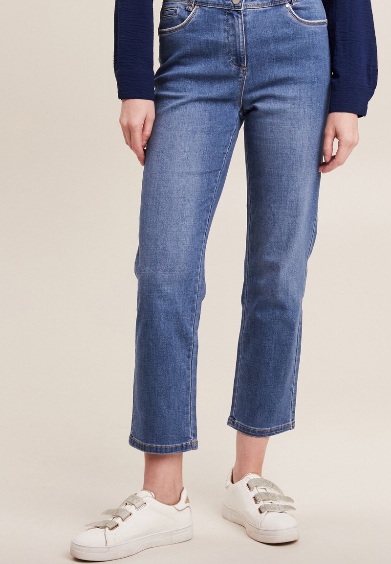 Blauwe denim jeans met een rechte pijp, vijf zakken en opgerolde zoom, gecombineerd met witte sneakers met grijze accenten.