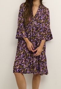 Vestido floral en púrpura oscuro con estampados de hojas rosas y verdes. Presenta mangas acampanadas, escote en V y diseño de falda con volantes. Tela ligera.
