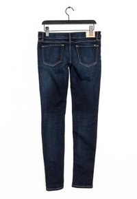 Jeans ajustados de color azul oscuro colgados en una percha negra, mostrados desde atrás con dos bolsillos traseros y detalles de costura visibles.