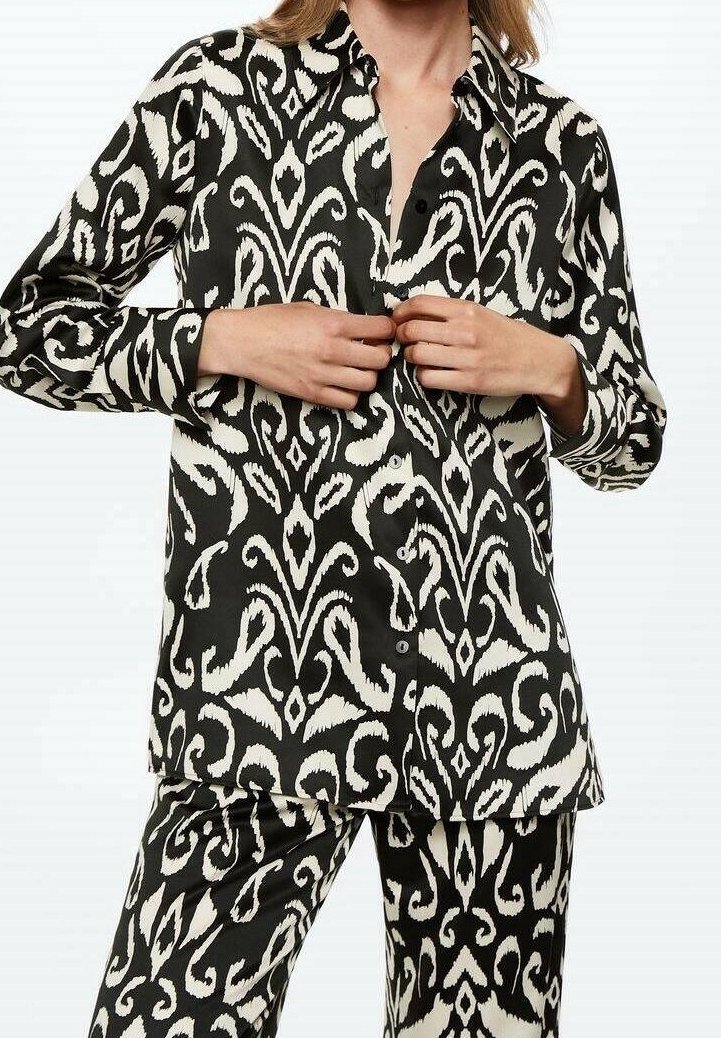 Blouse à motif noir et crème avec un design à boutons-pression, manches longues et coupe ample, assortie à un pantalon à motif similaire.
