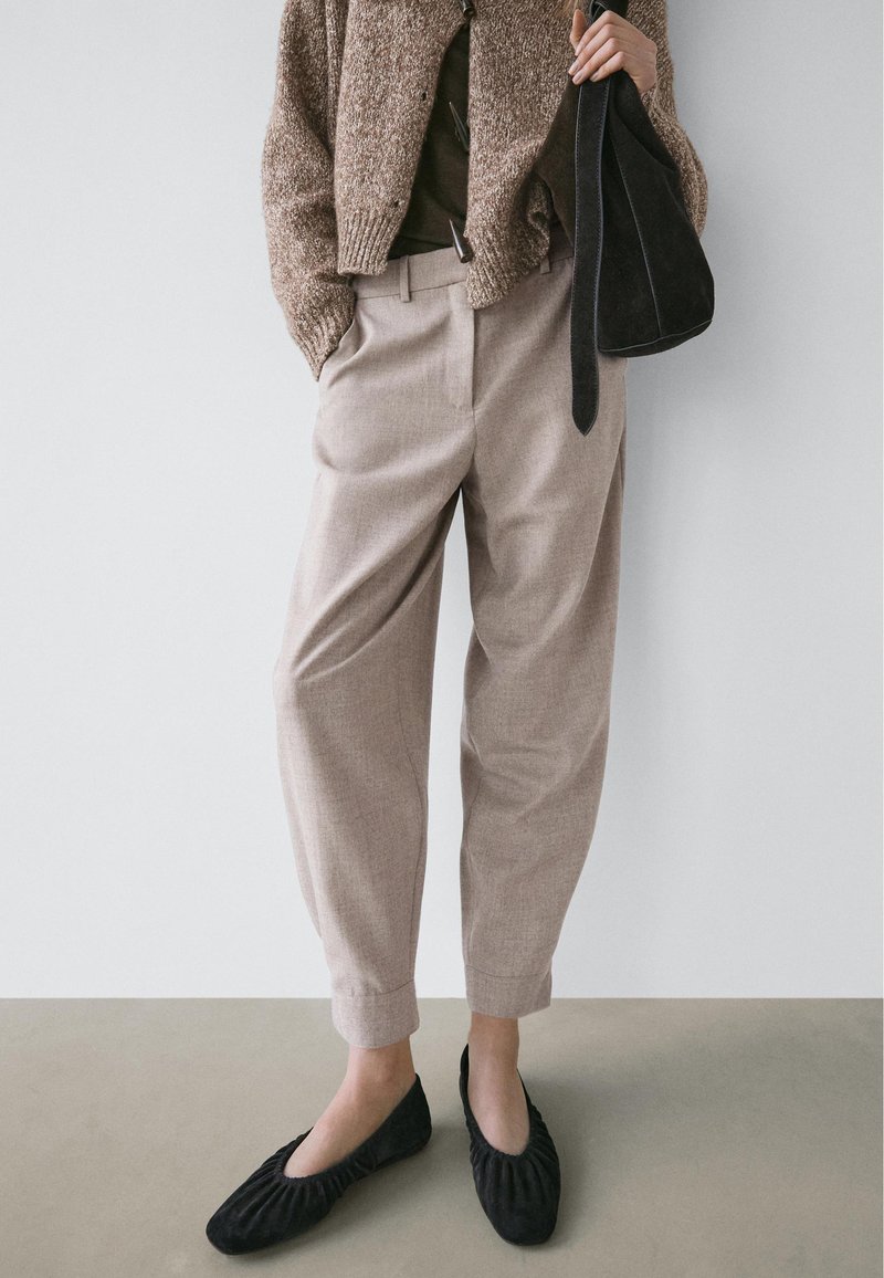 Lysebeige højtaljede bukser med afslappet pasform, kombineret med en tekstureret brun strikket cardigan og sorte flade sko med rynket detalje.