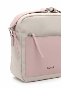 Beige fabric bag with pink leather accents, featuring a front zip pocket, a simple rectangular shape, and a logo embossed on the front.