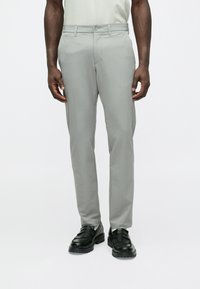 Pelēkas pieguļošas bikses ar gludu tekstūru, aiztais�āmas ar pogu, ar jostas cilpām un kabatām. Kombinētas ar melniem loaferi tipa apaviem.