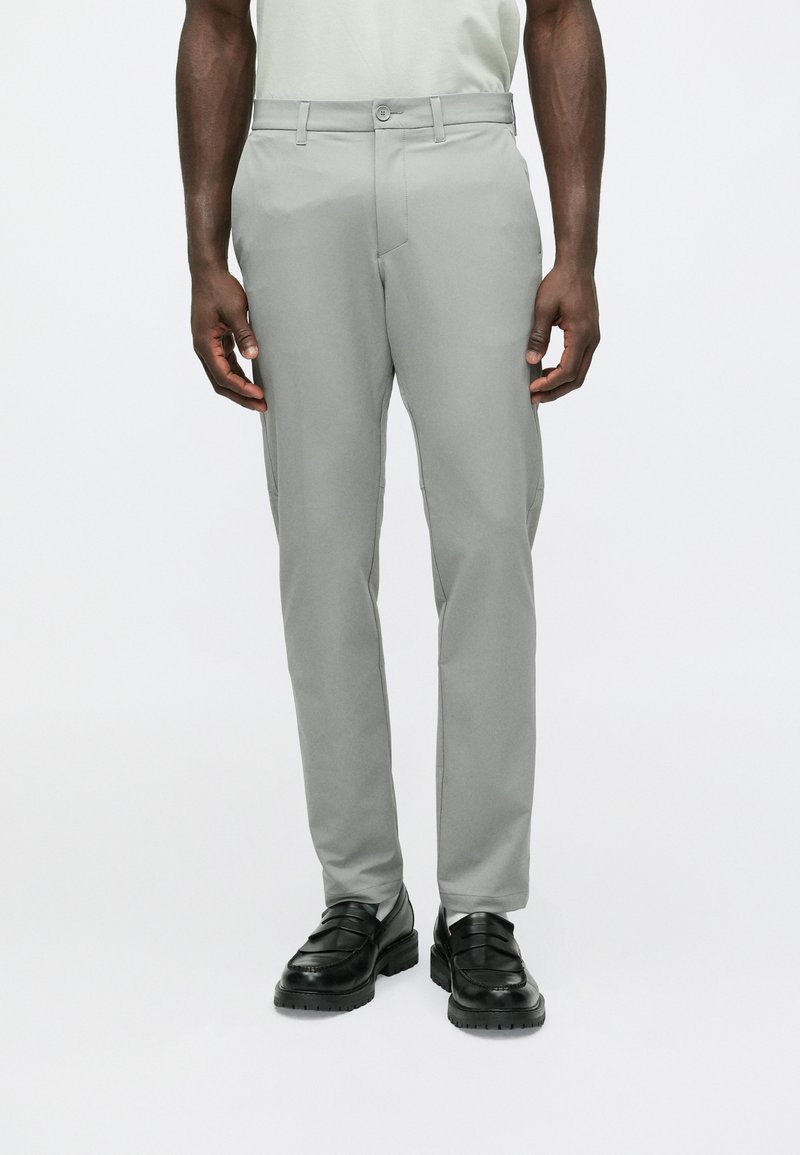 Pelēkas pieguļošas bikses ar gludu tekstūru, aiztaisāmas ar pogu, ar jostas cilpām un kabatām. Kombinētas ar melniem loaferi tipa apaviem.