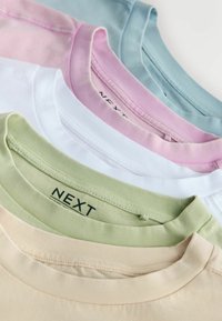 Pile de cinq t-shirts à col rond dans des couleurs pastel : beige, vert clair, blanc, rose et bleu clair, avec une étiquette de marque NEXT visible.