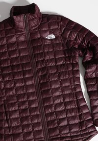 Giacca isolante bordeaux con design a trapunta, colletto alto, zip frontale e logo sul lato sinistro del petto. Tessuto liscio e lucido.