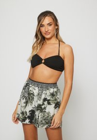 Top de bikini negro texturizado con un frente retorcido y detalle en forma de llave, combinado con pantalones cortos claros estampados que presentan palmeras y tigres.